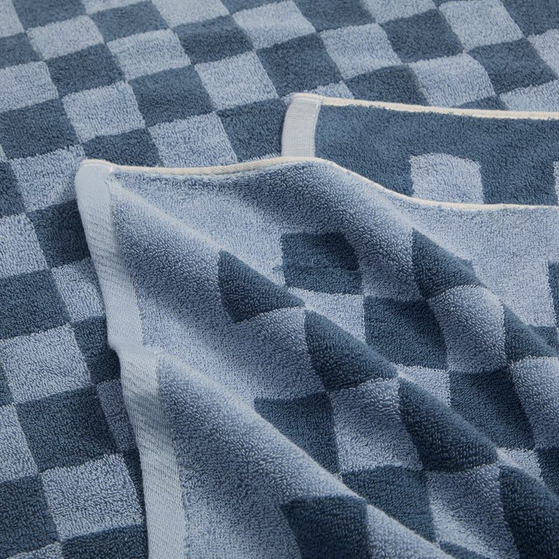 Close-up of a REDKISS blue checkerboard 100% cotton bath towel from a 2-pack, showing alternating muted blue squares, soft textured fabric and light-colored edge binding. #color_blue